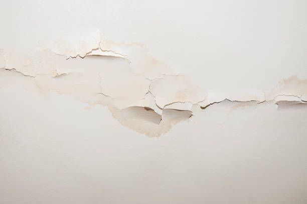 White wall with peeling paint, cracks, and water damage in close-up view of interior surface.