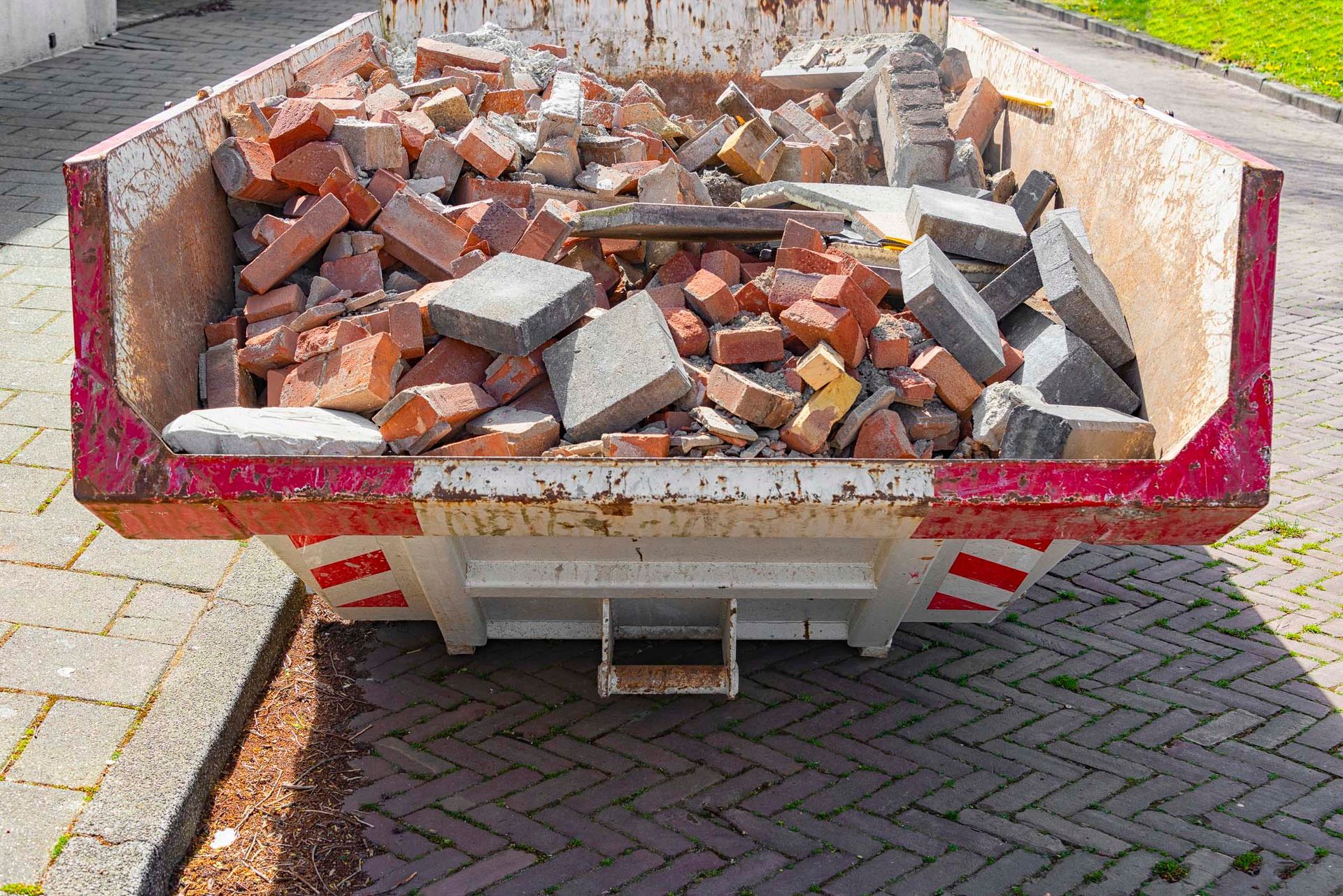 A dumpster filled with bricks and concrete is parked on a sidewalk.