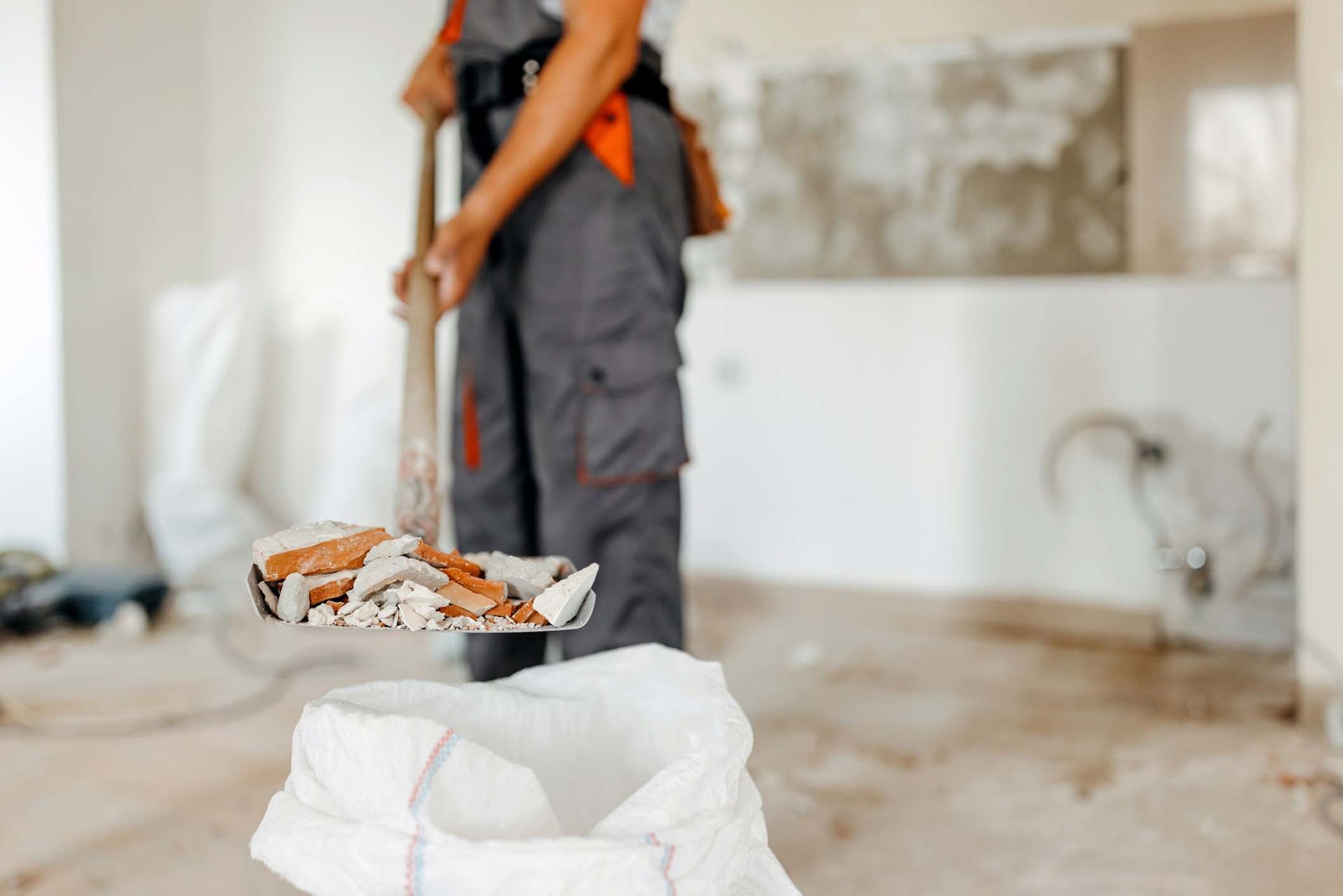 A man is cleaning a room with a mop and a bag of trash.