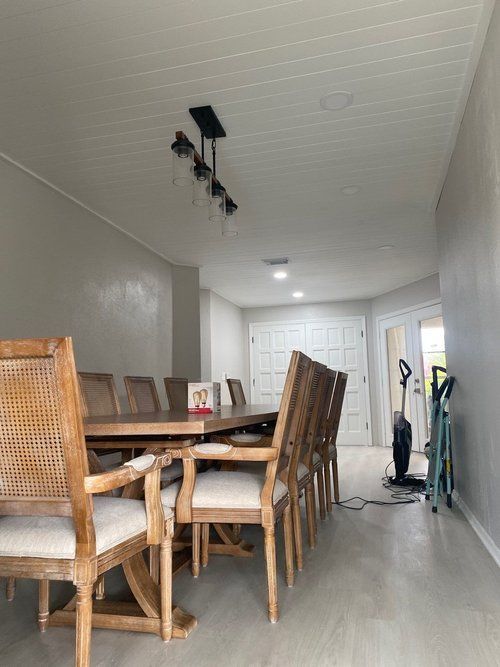 A dining room with a long table and chairs and a vacuum cleaner.
