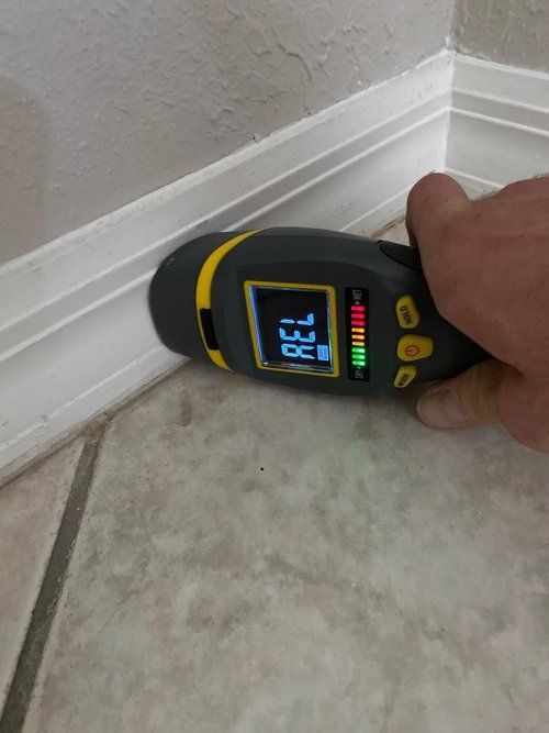 A person is using a moisture meter on a tiled floor.