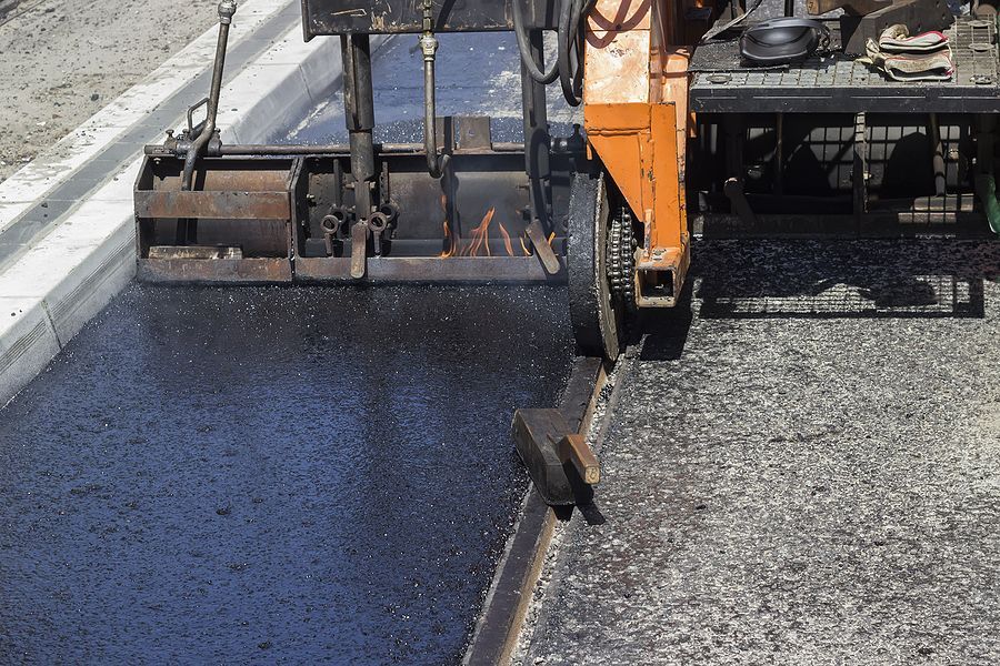 Road paving machine laying fresh black asphalt beside a curb
