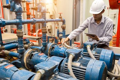 Man in hard hat inspecting industrial pumps with a tablet.