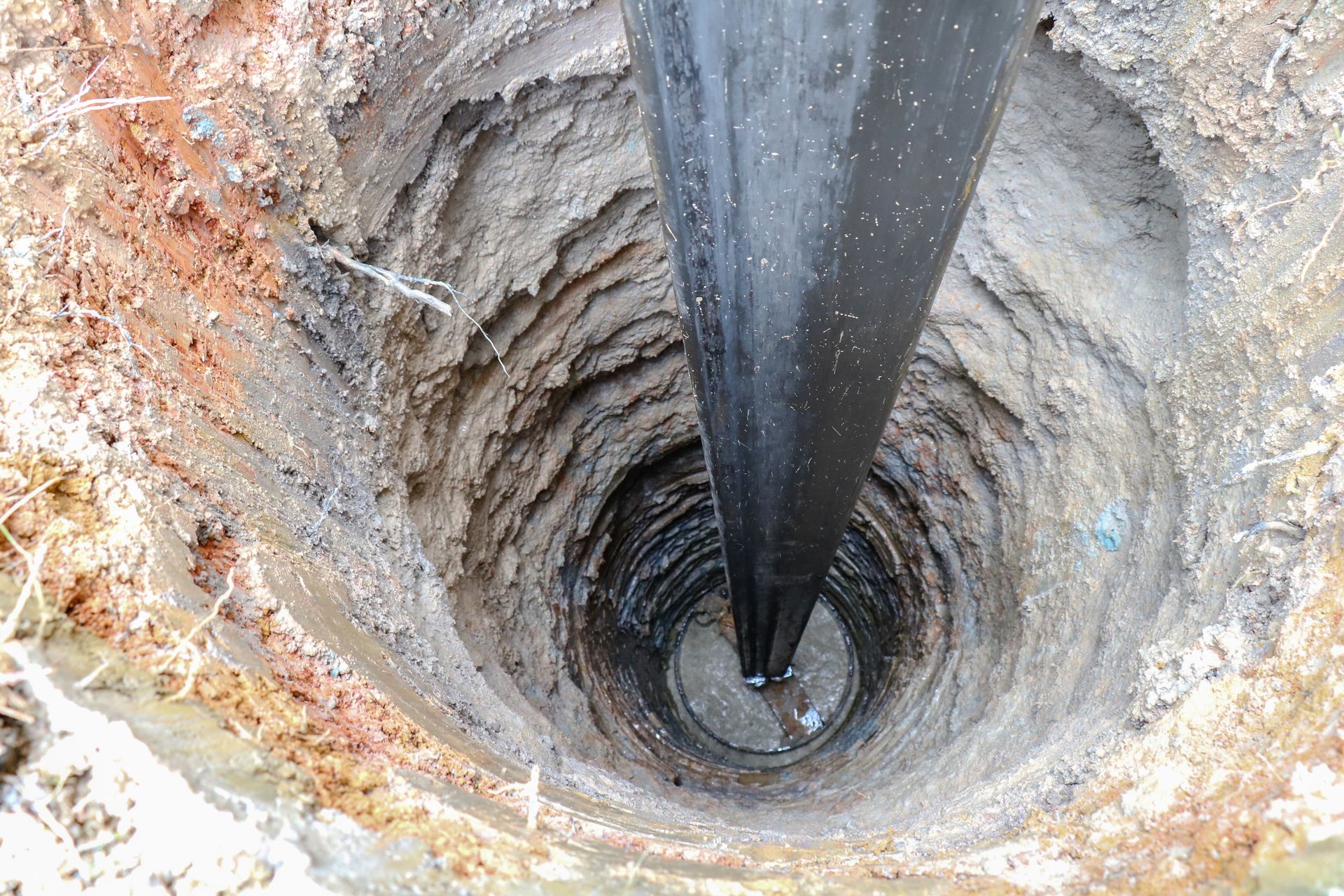 Pipe inserted vertically into a deep excavated hole or well shaft with exposed soil layers.
