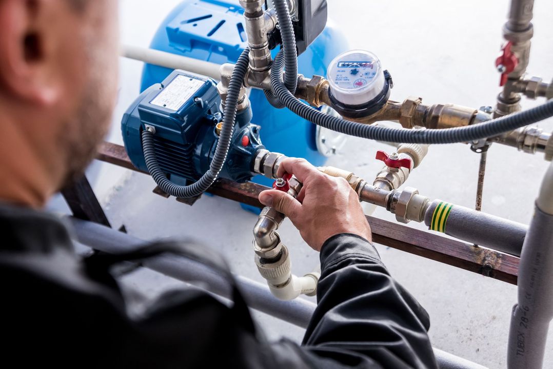 Person adjusting a valve on a water pump system, outdoors.
