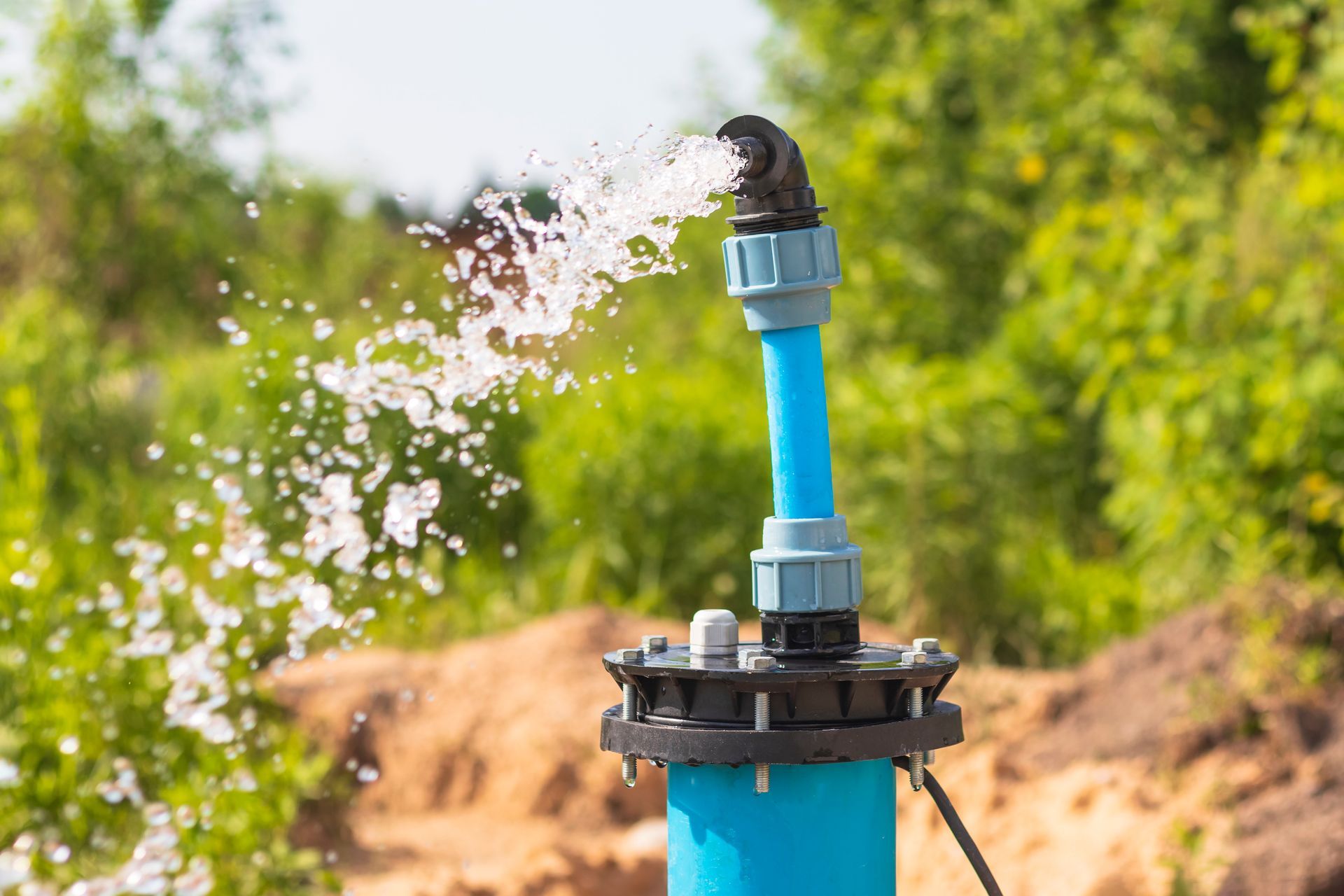 Water gushing from a blue well pipe with a black elbow joint, outdoors.