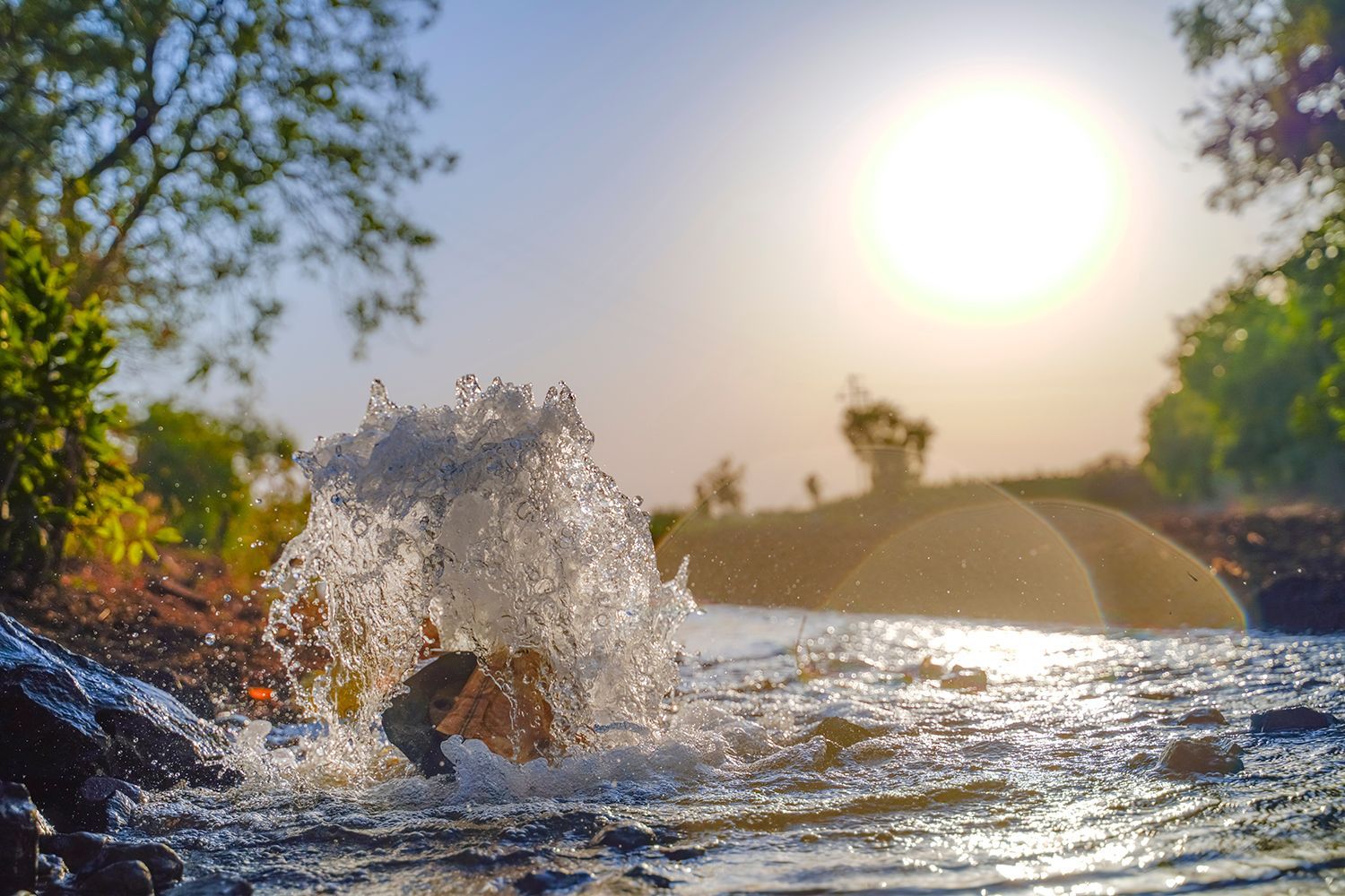Water bursts from a newly drilled ground opening as sunlight shines over the scene.