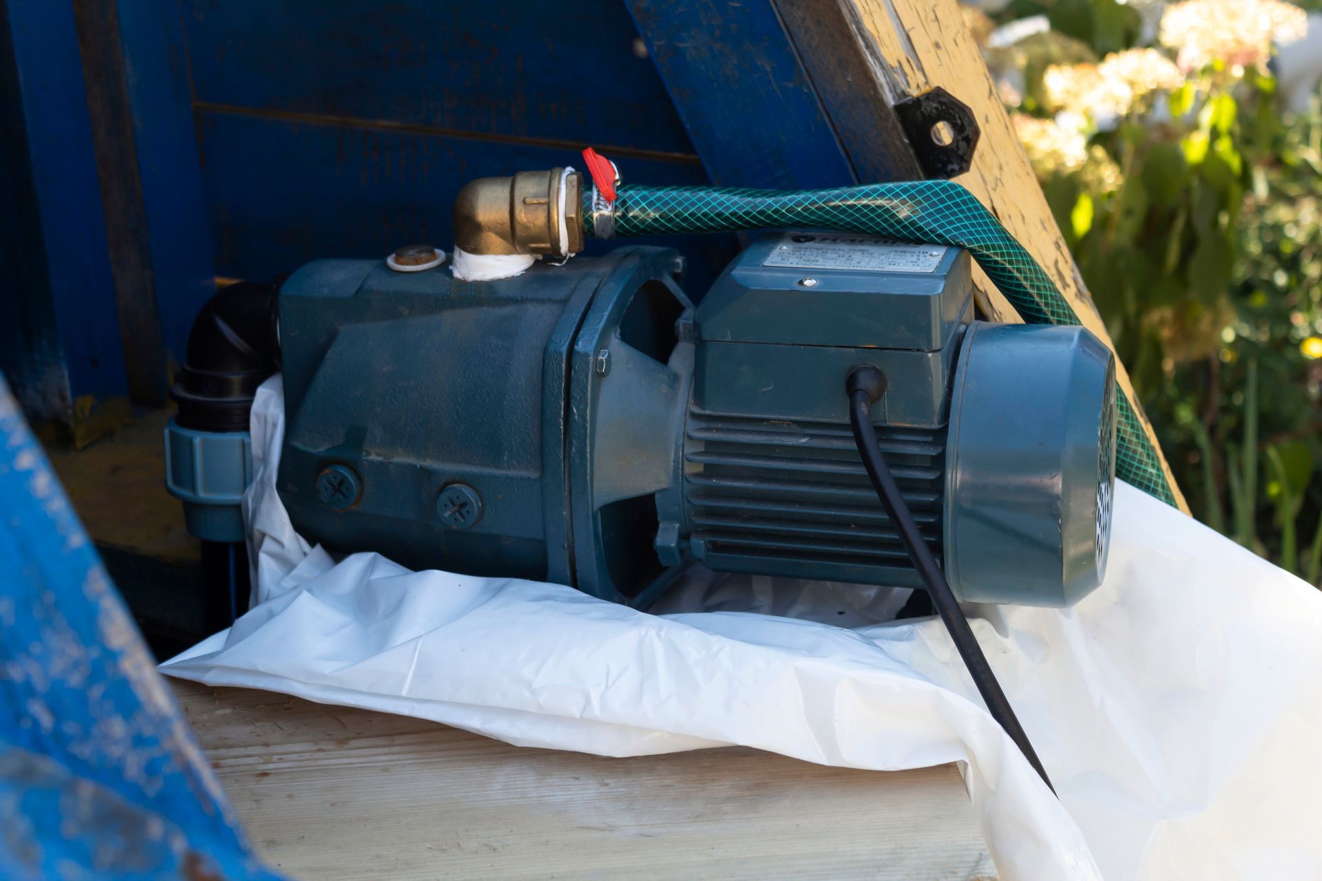 Blue water pump with brass fitting, resting on a white surface, within a blue structure, with green hose.