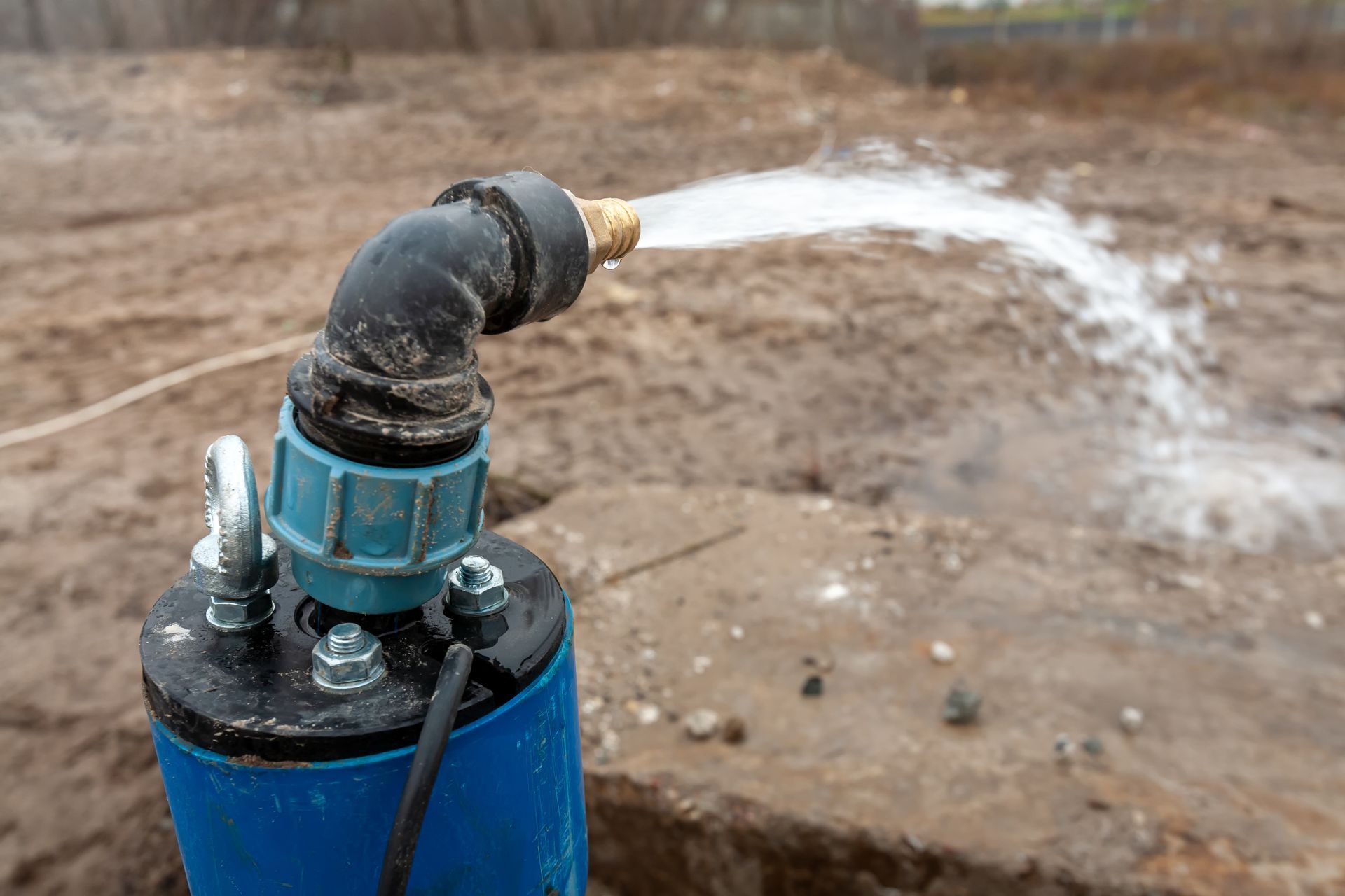 Blue water pump spraying water onto dirt ground.