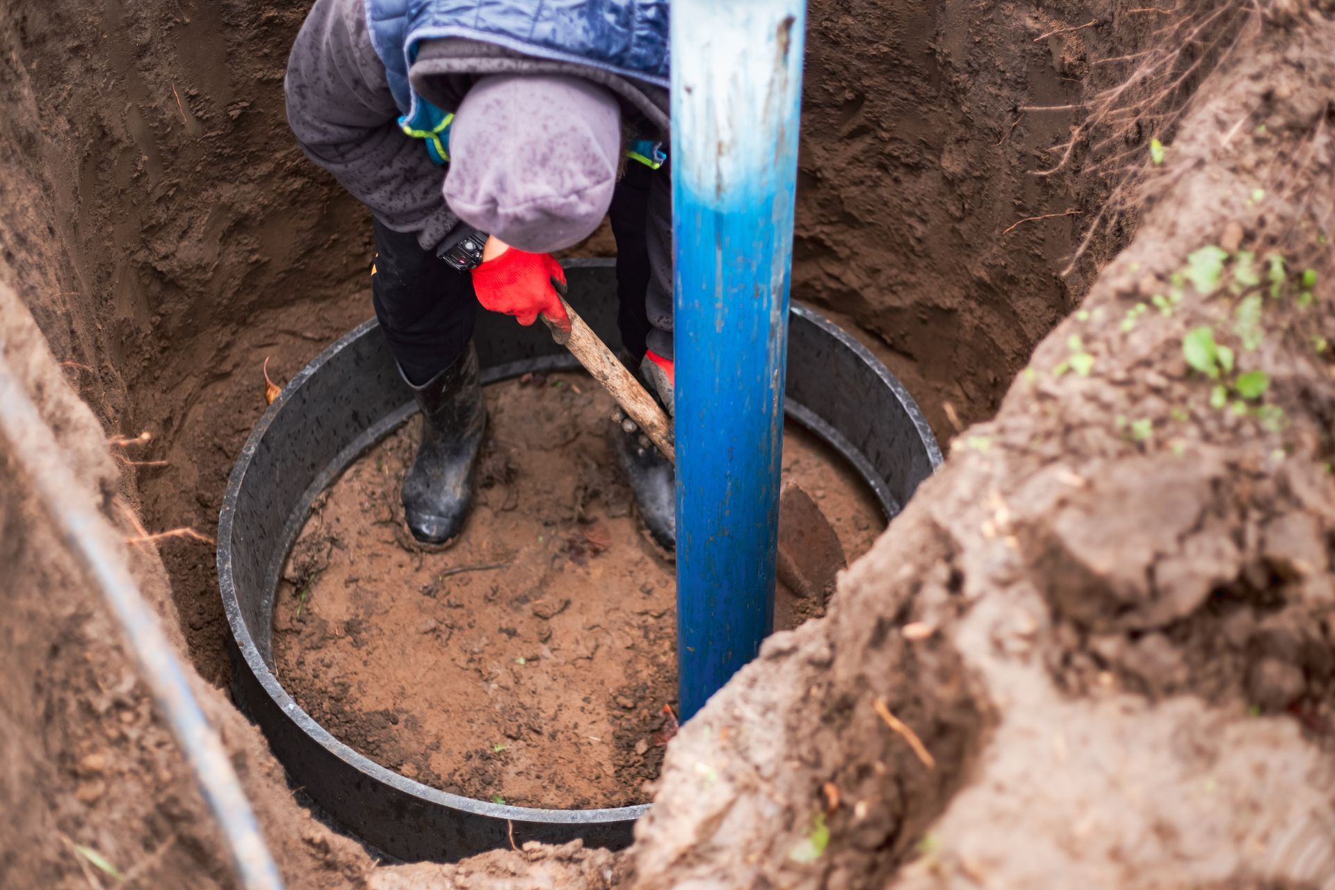 Person in a trench shovels dirt near a large circular pipe.