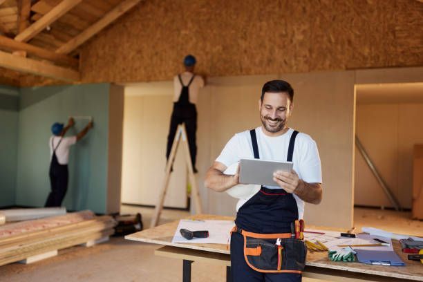 A construction worker using a digital tablet while working inside of a house under construction.