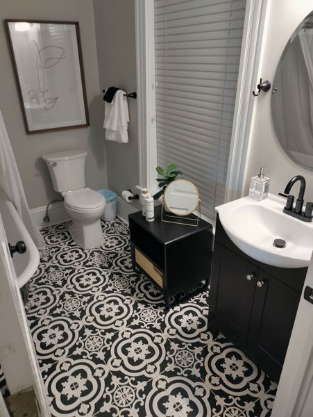 Bathroom with black and white patterned floor tiles, a toilet, vanity, shower, and artwork.