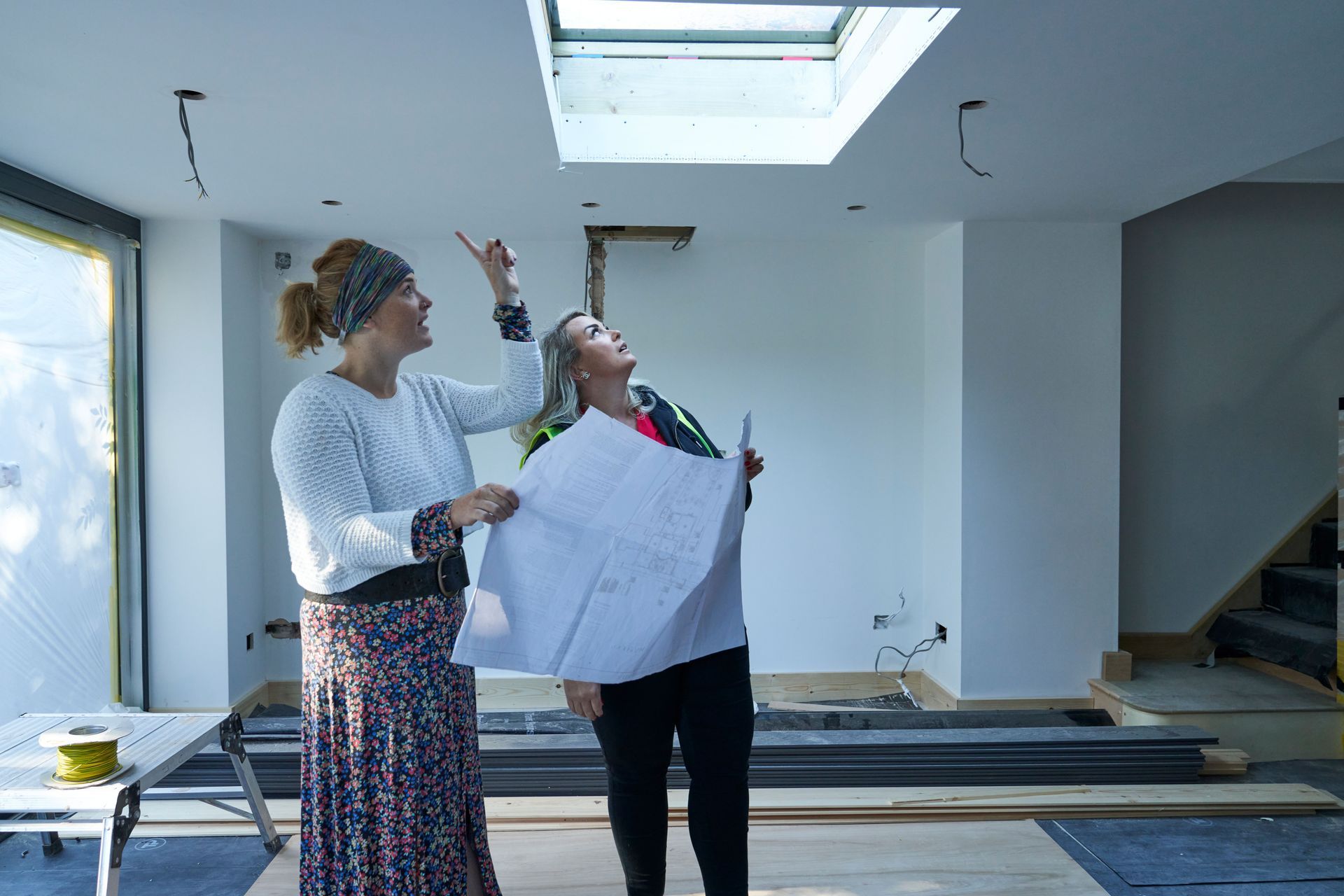 A contractor and a client stand in an extension project while looking up at the progress of the job.