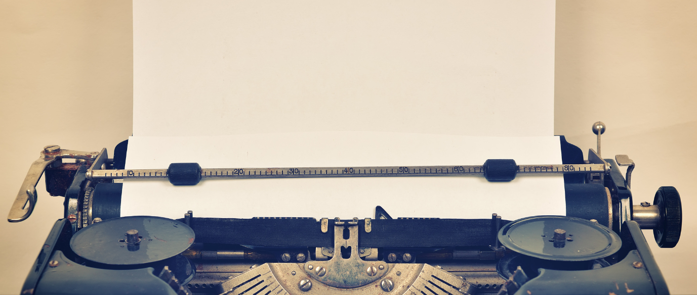 Close-up of an antique typewriter with a blank white sheet of paper, lit by warm light.