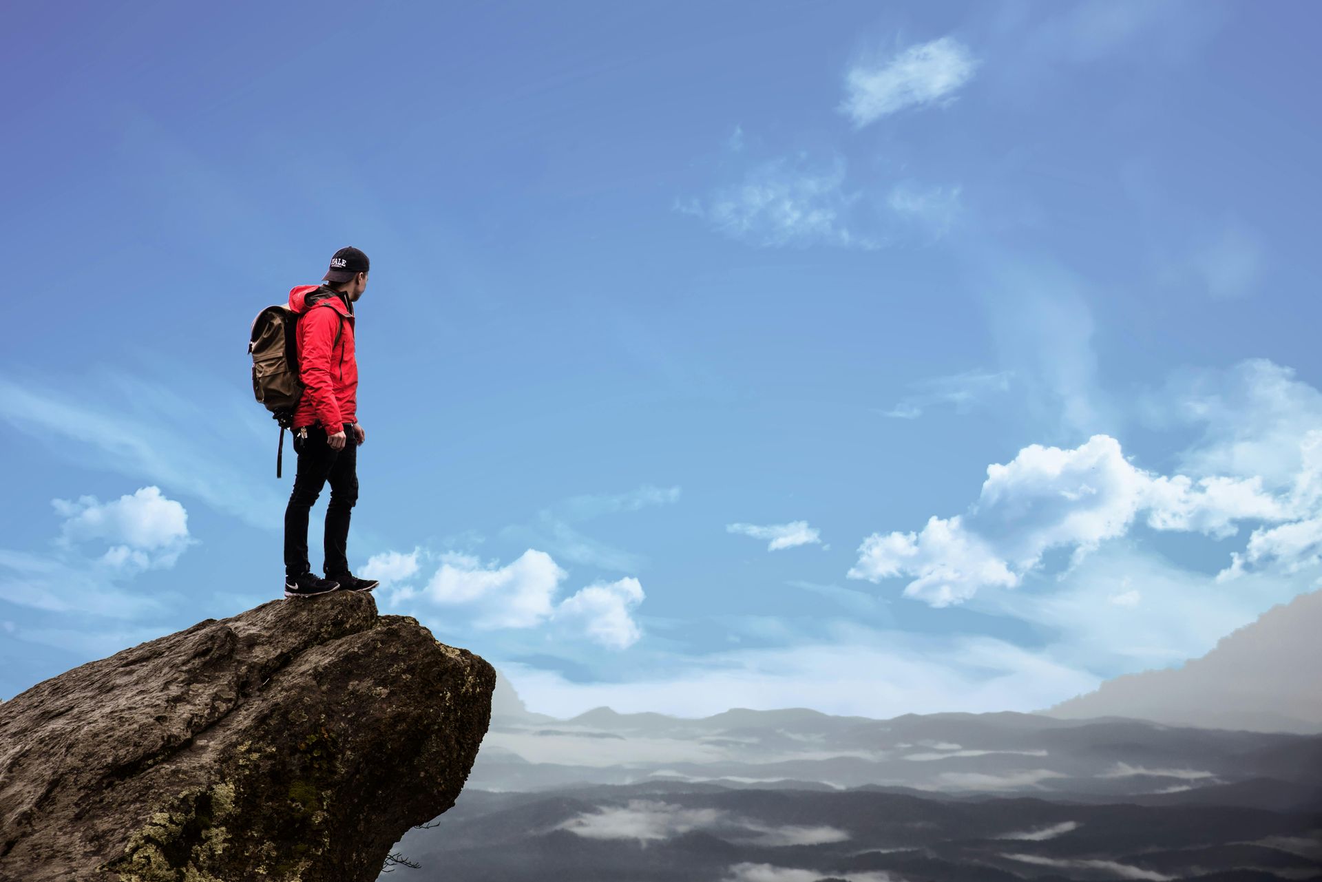 A man with a backpack is standing on the edge of a cliff.
