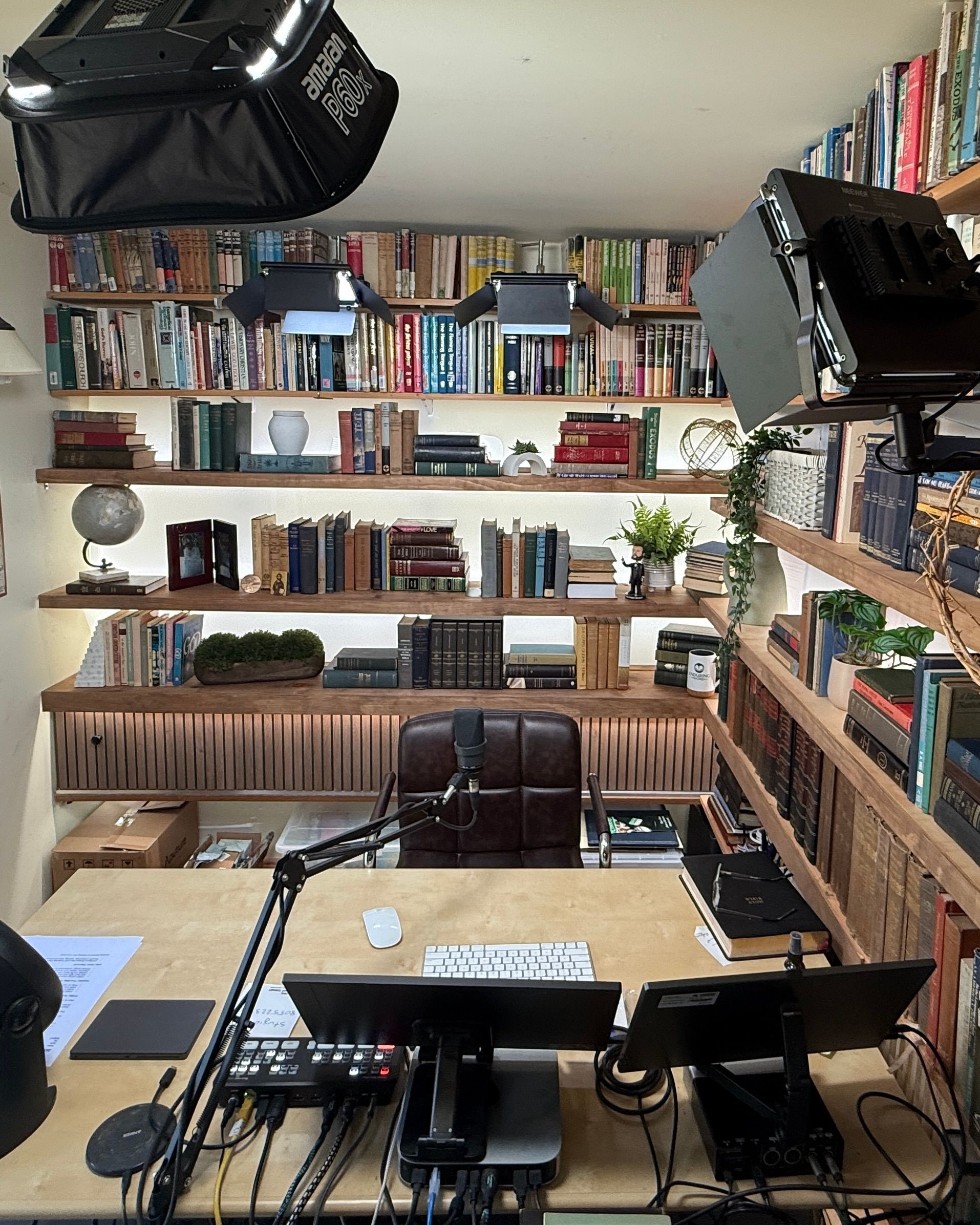 Home office with desk, shelves of books, two monitors, and recording equipment.