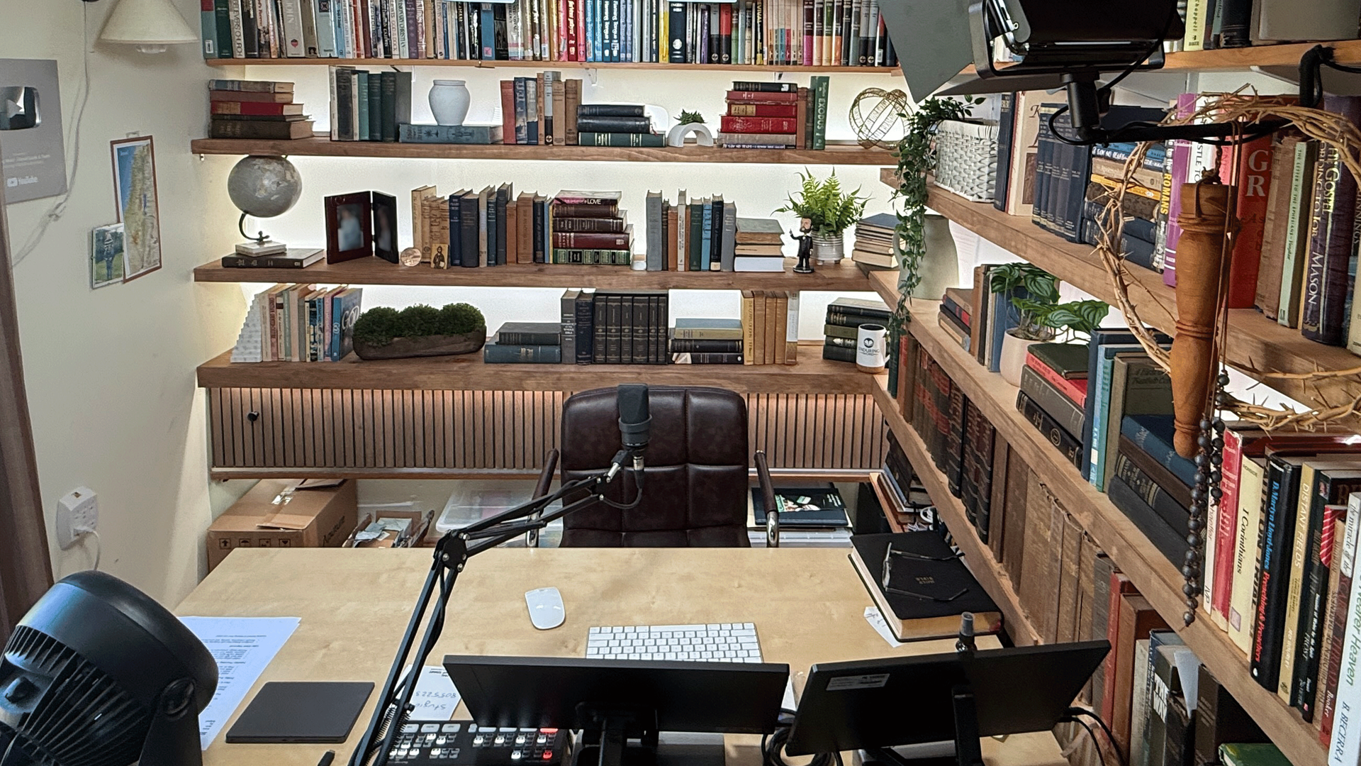 Cozy home office with wooden shelves full of books, desk, mic, and recording equipment.