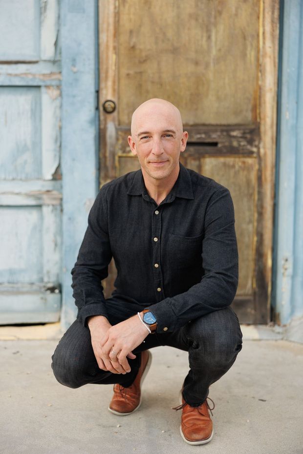 Greg Pickard is wearing a black shirt and is sitting in front of a white garage door.
