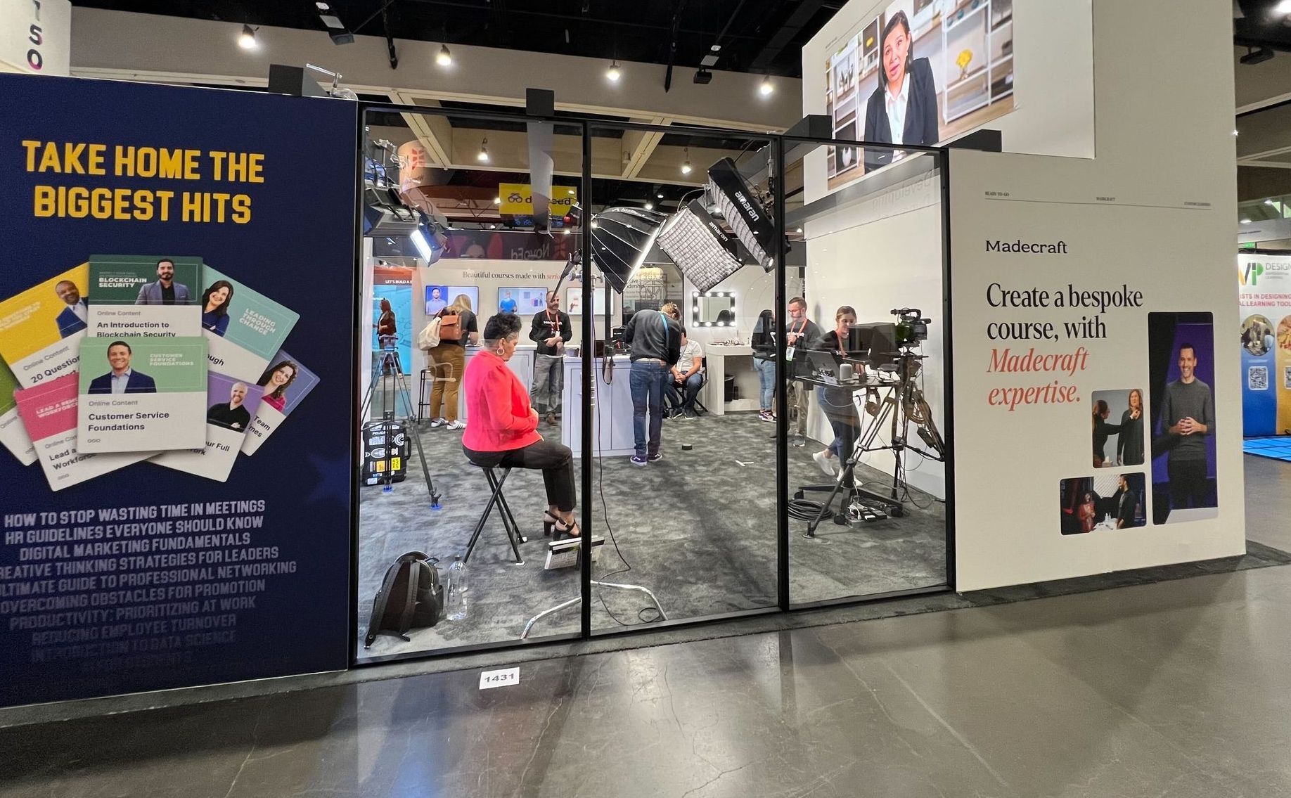 A woman is sitting in front of a sign that says take home the biggest hits.