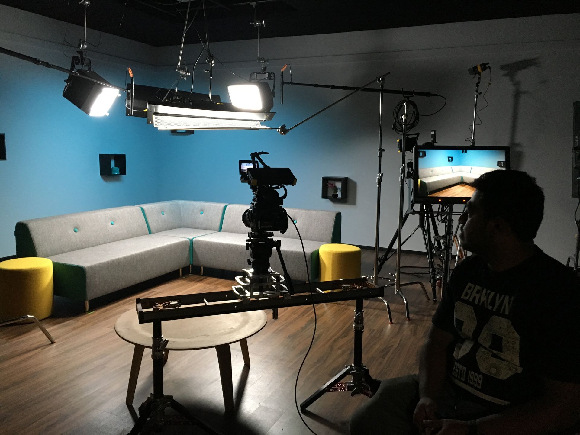 Film set with camera on slider, sofa, lights, and crew member watching.
