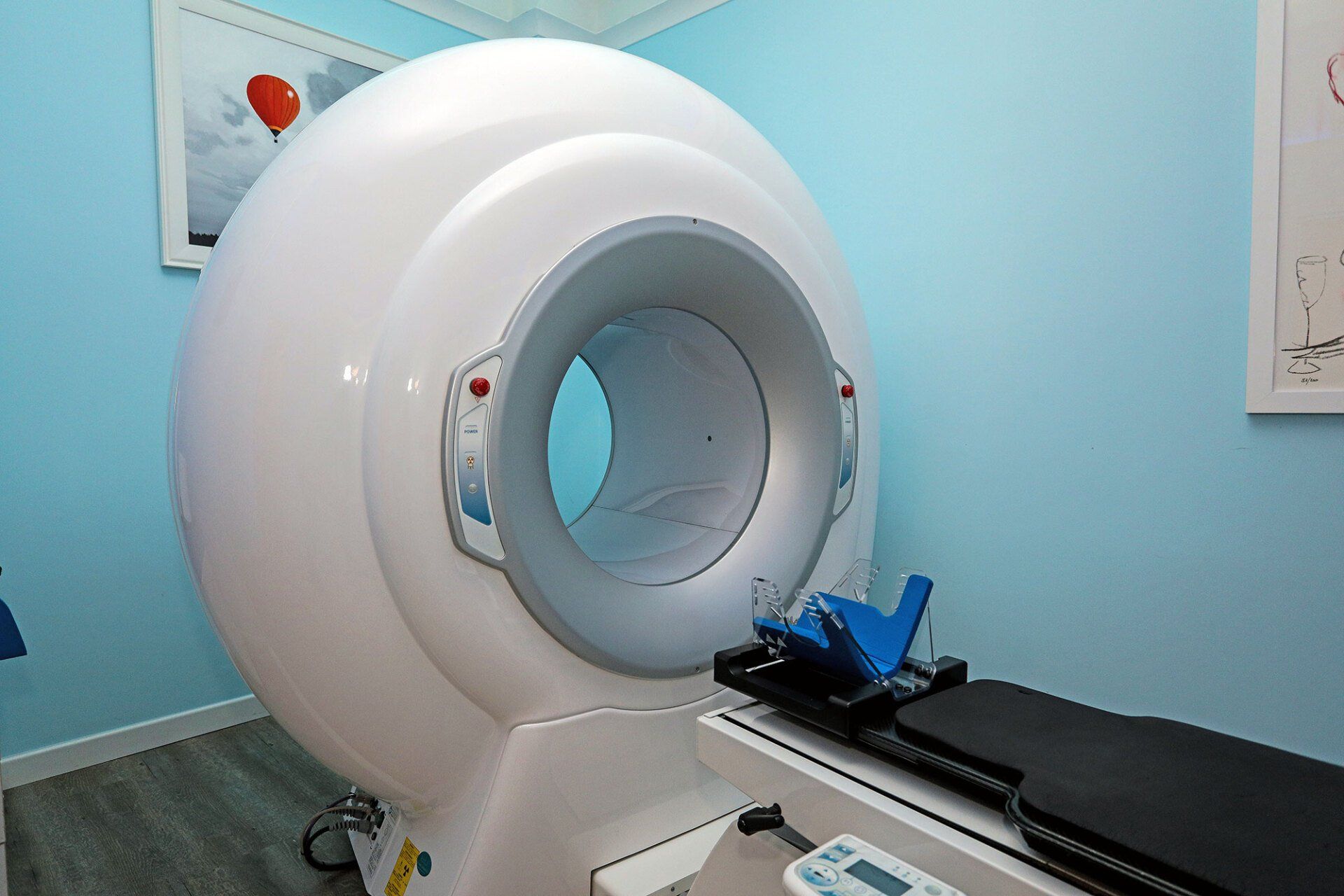 Uno scanner per immagini medicali con un grande involucro sferico e un lettino per il paziente in una stanza azzurra.
