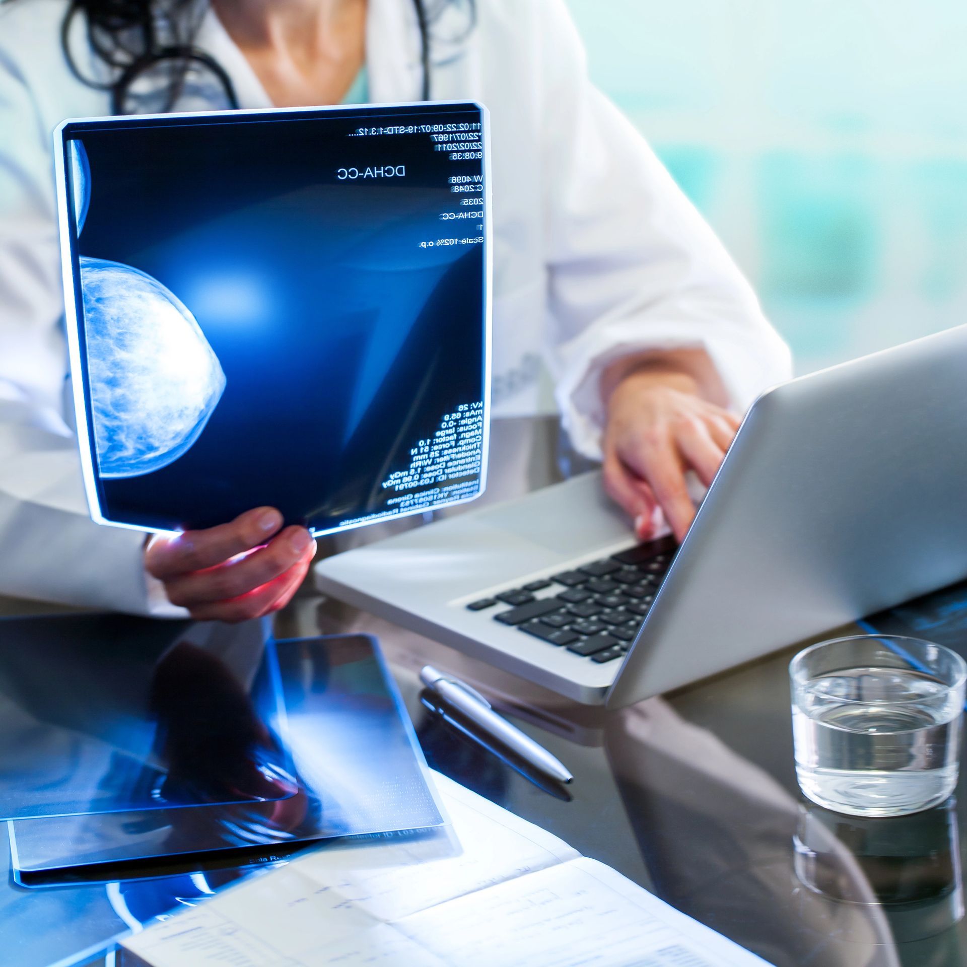 Un operatore sanitario in camice bianco esamina una mammografia utilizzando un computer portatile.