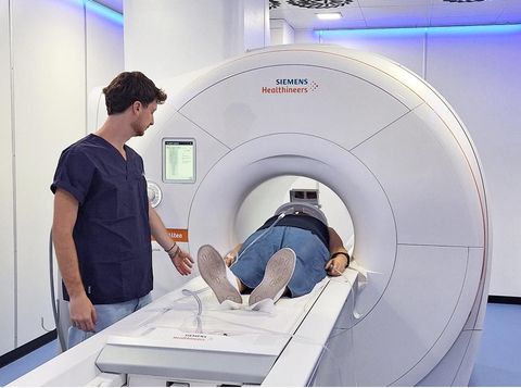 In una luminosa stanza clinica, un tecnico prepara un paziente sdraiato sul lettino di una TAC.