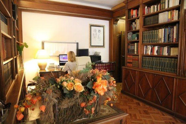 Una persona lavora al computer in un accogliente studio arredato con librerie in legno scuro e una grande composizione floreale sulla parete di fronte.