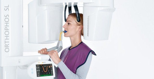 Una persona con indosso un grembiule di piombo posizionata all'interno di un apparecchio radiografico dentale Orthophos SL per una scansione.