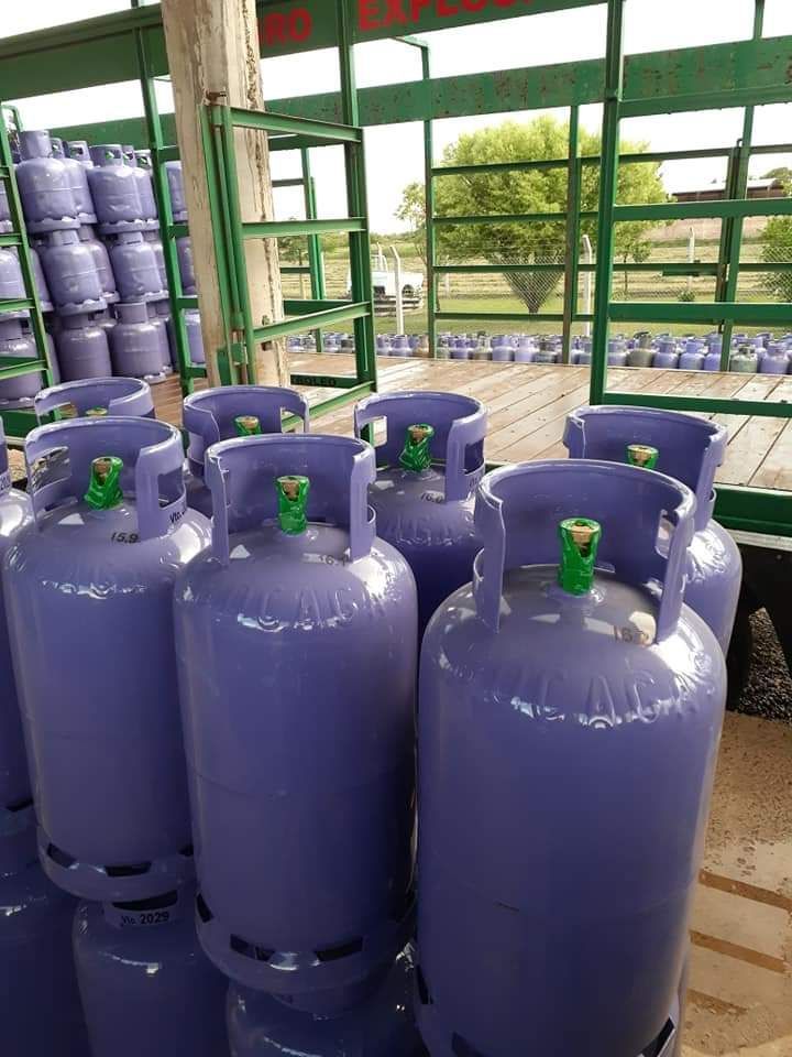 Filas de bombonas de gas de color púrpura almacenadas en un almacén al aire libre bajo una estructura metálica.