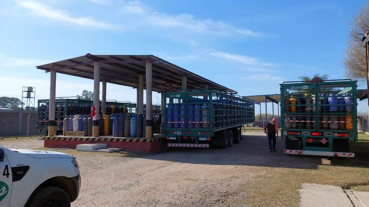 Camiones cargados con bombonas de gas estacionados bajo una marquesina industrial al aire libre en un día soleado.