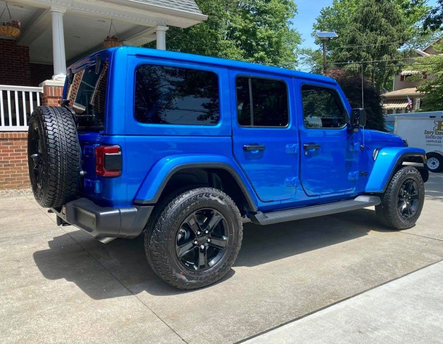 A blue jeep is parked in a driveway in front of a house.