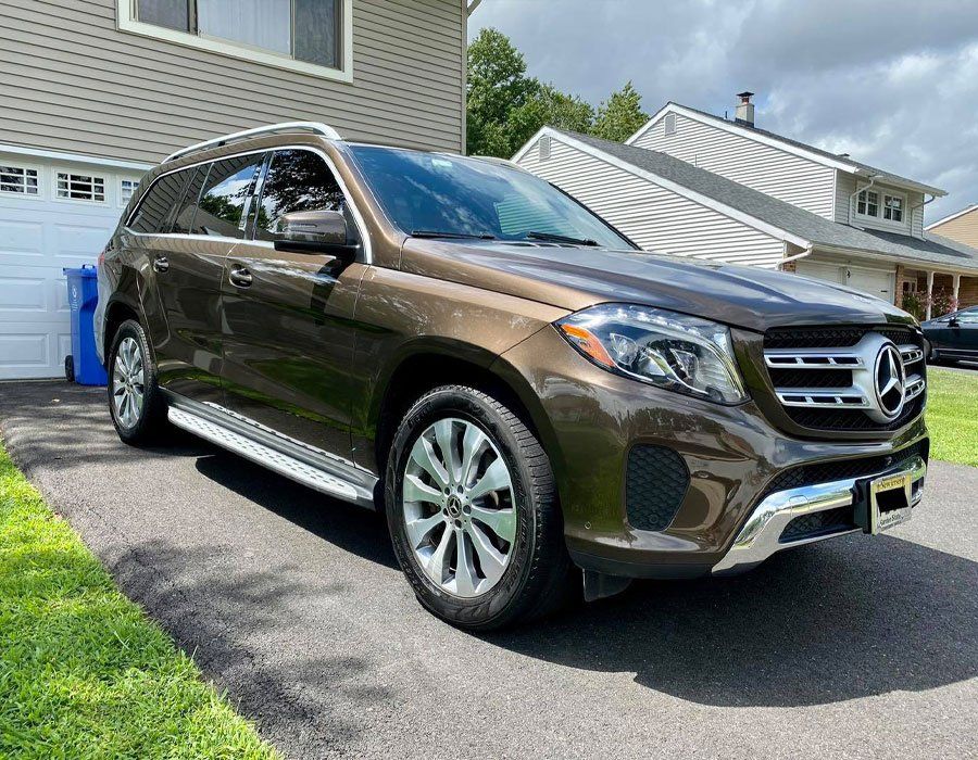 A brown mercedes benz gls class is parked in front of a house.