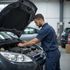 Mechanic in blue uniform repairs car engine in a garage; focused expression.