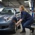 Woman in blue workwear checking the tire of a blue car in a garage.