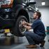 Mechanic in blue shirt crouches, tightening lug nuts on a vehicle's tire in a garage setting.
