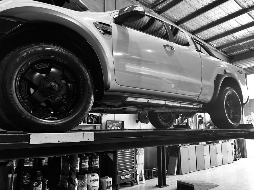 Truck on a car lift in a repair shop, seen from a low angle. Black and white.