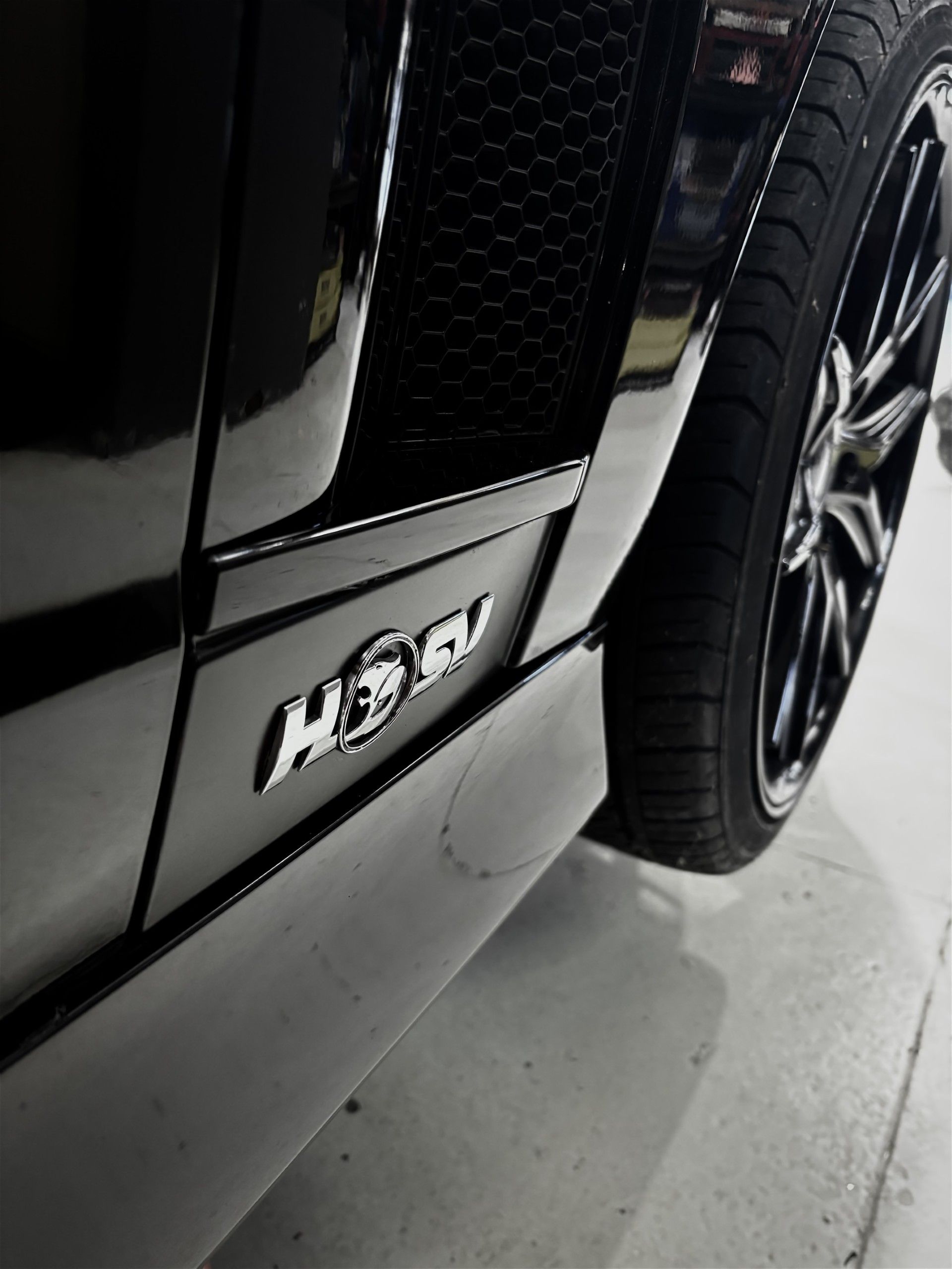 Black car side with chrome H3 logo on a white floor, showing a tire and wheel.