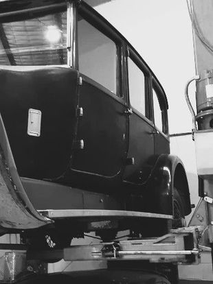 Black and white photo of an antique car on a lift inside a garage.
