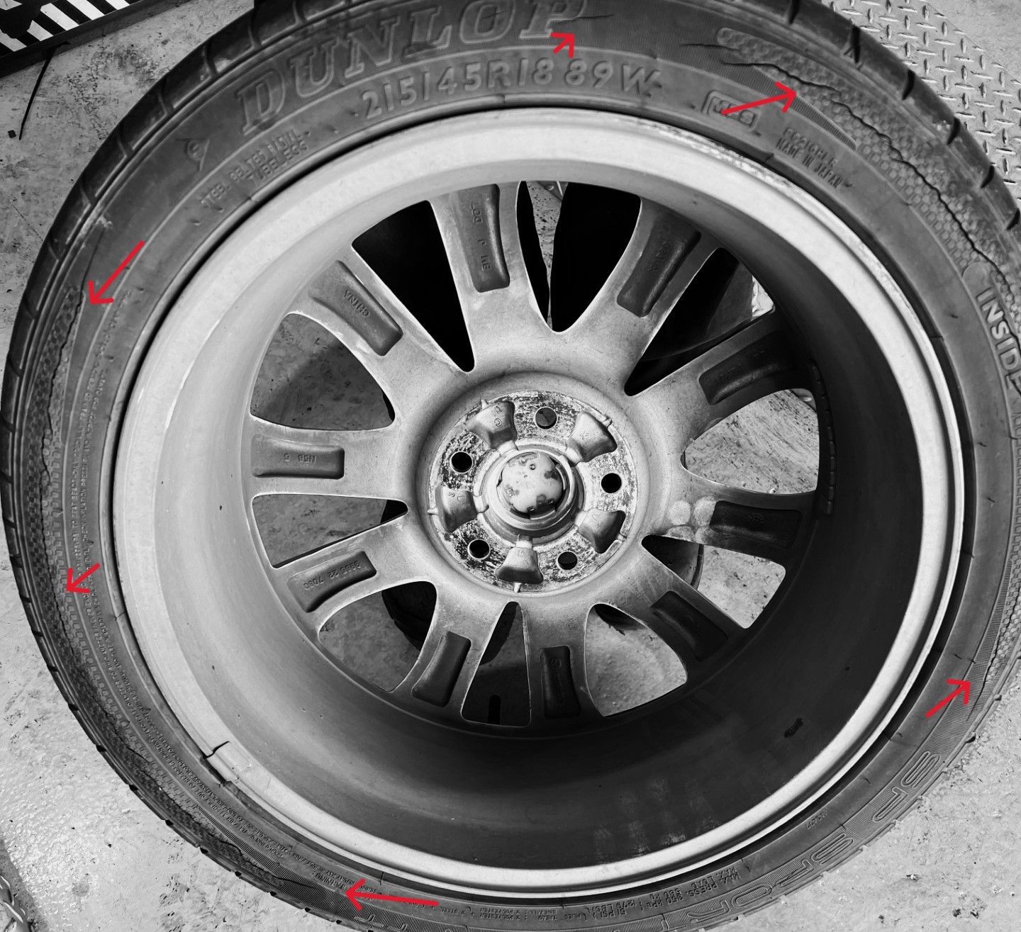 Close-up of a tire with multiple cracks. The tire is mounted on a silver alloy wheel.