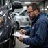 Mechanic inspecting a car, writing on a clipboard in a garage.