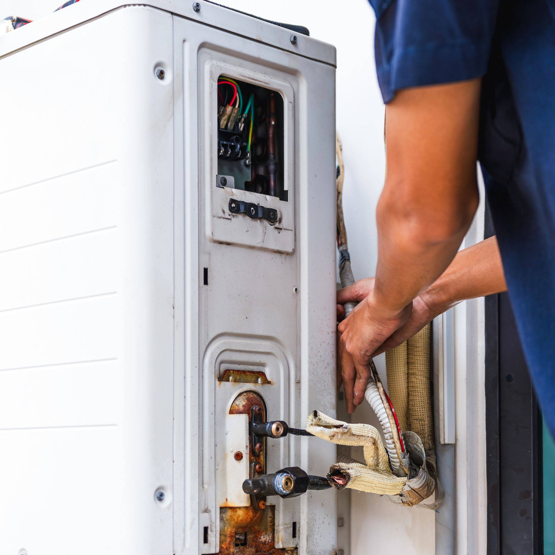 Person repairs outdoor air conditioning unit; hands working on pipes and wires.