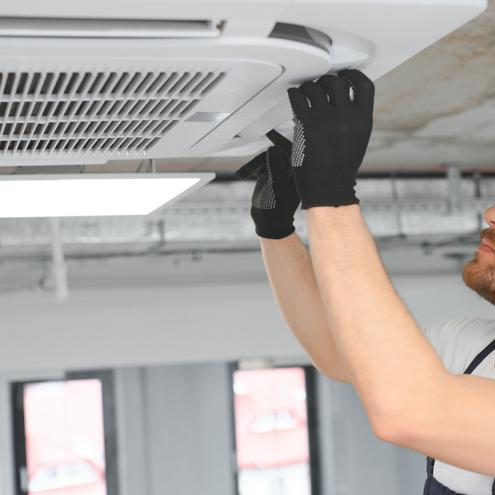 Person in black gloves fixing an air conditioning unit on a ceiling with a screwdriver.