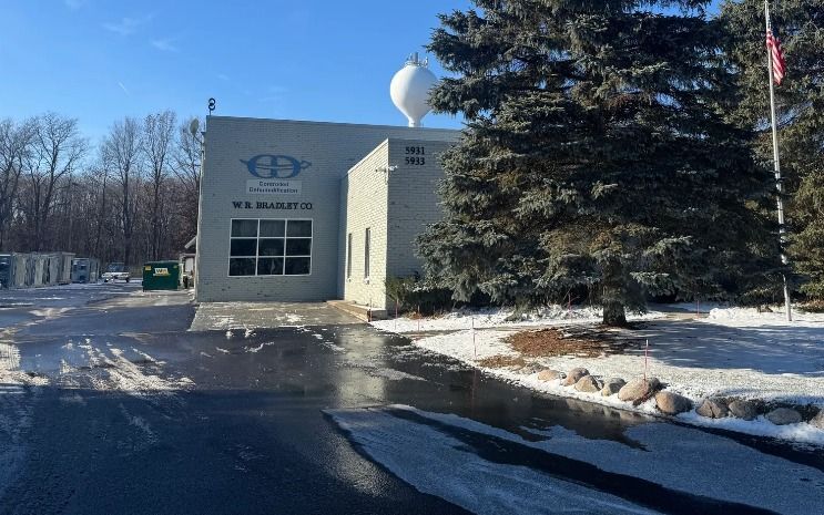 A large white building with a water tower in the background is surrounded by snow and trees.