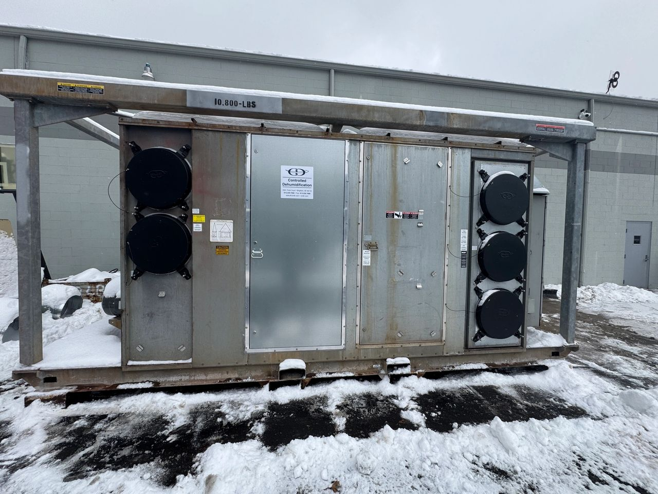 A stainless steel building is sitting in the snow in front of a building.