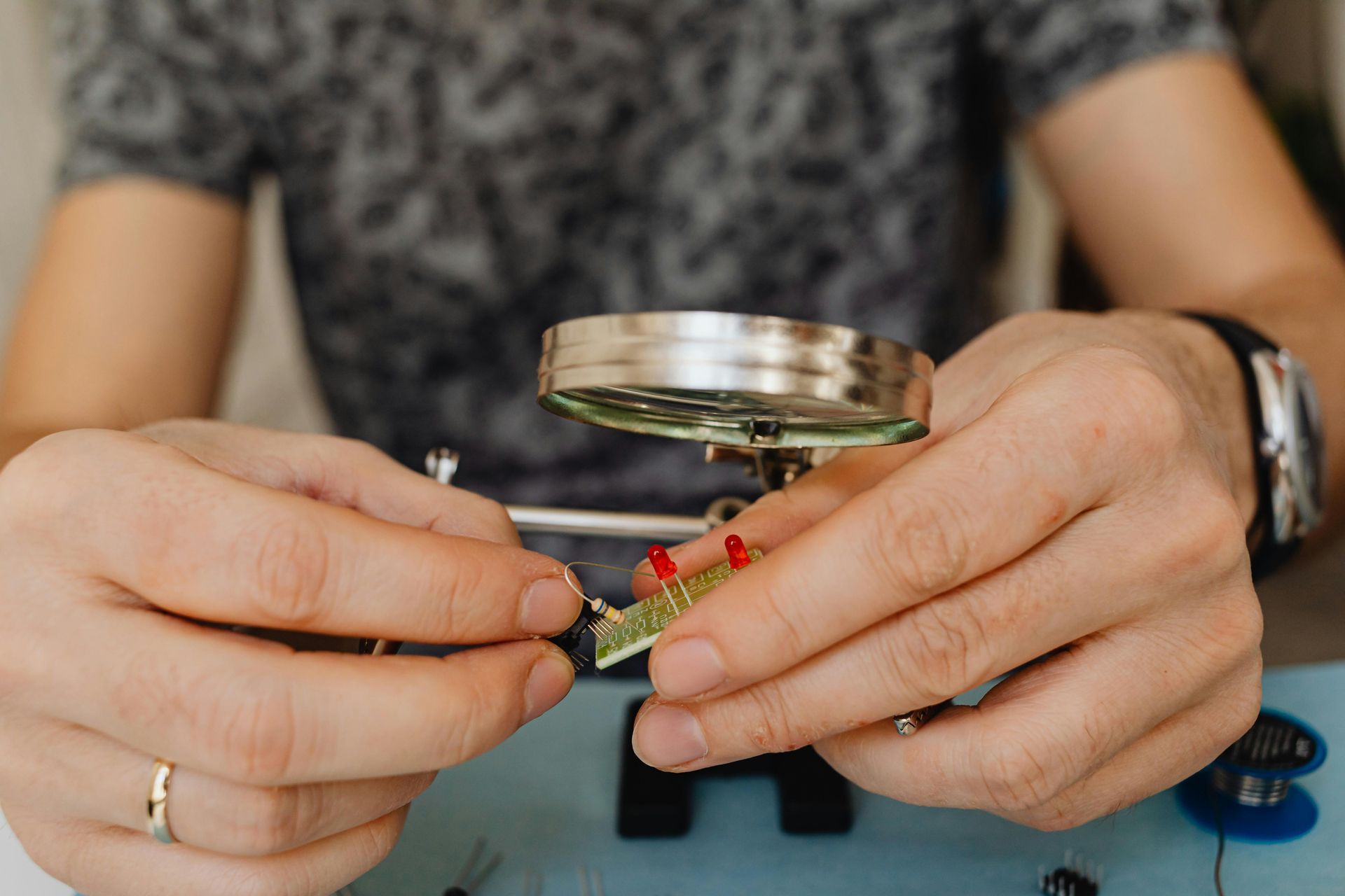 A man is working on a circuit board with a magnifying glass.