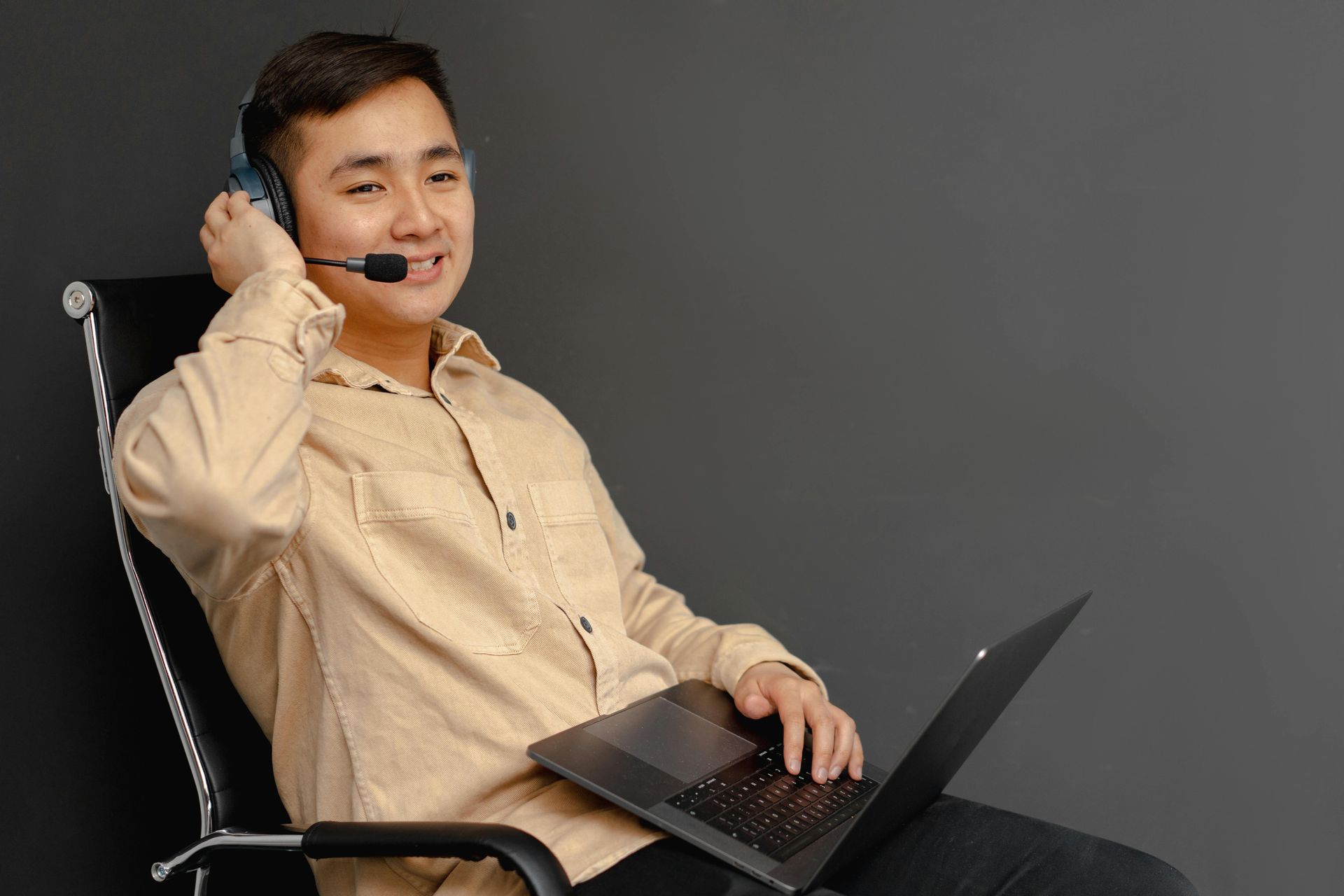 A man wearing headphones and a microphone is sitting in a chair with a laptop.