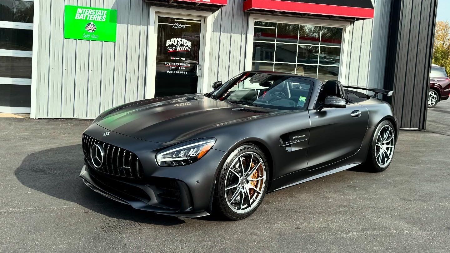 Black Mercedes-AMG GT roadster parked outside a garage with a green sign.
