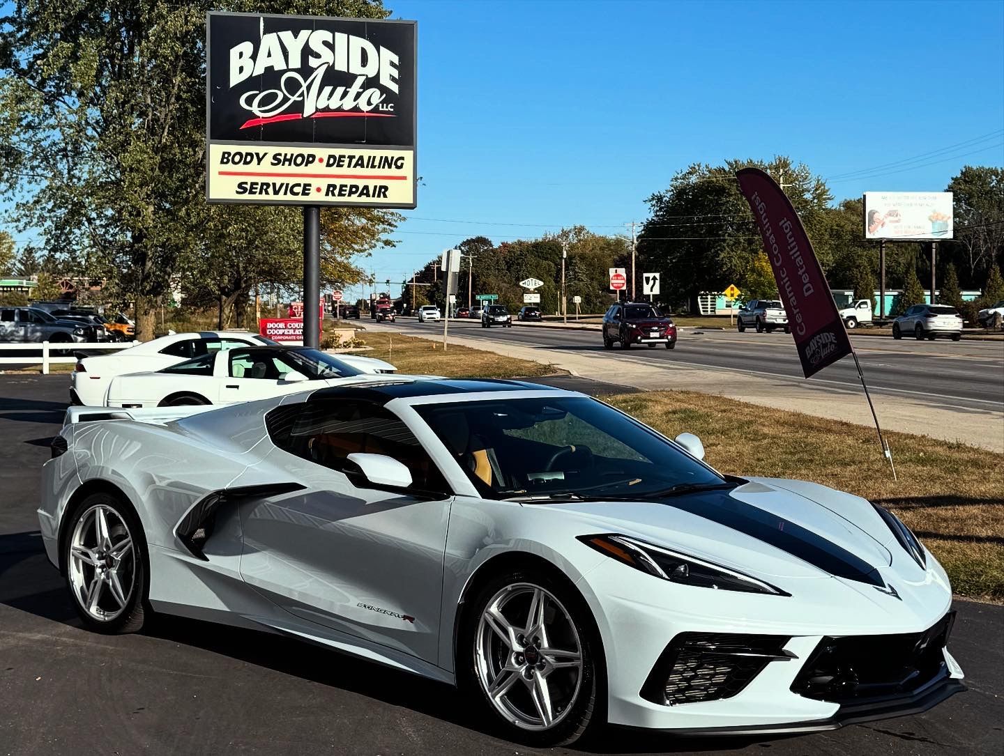 Silver Corvette in front of Bayside Auto shop. Black stripe on the hood. Body shop sign visible.