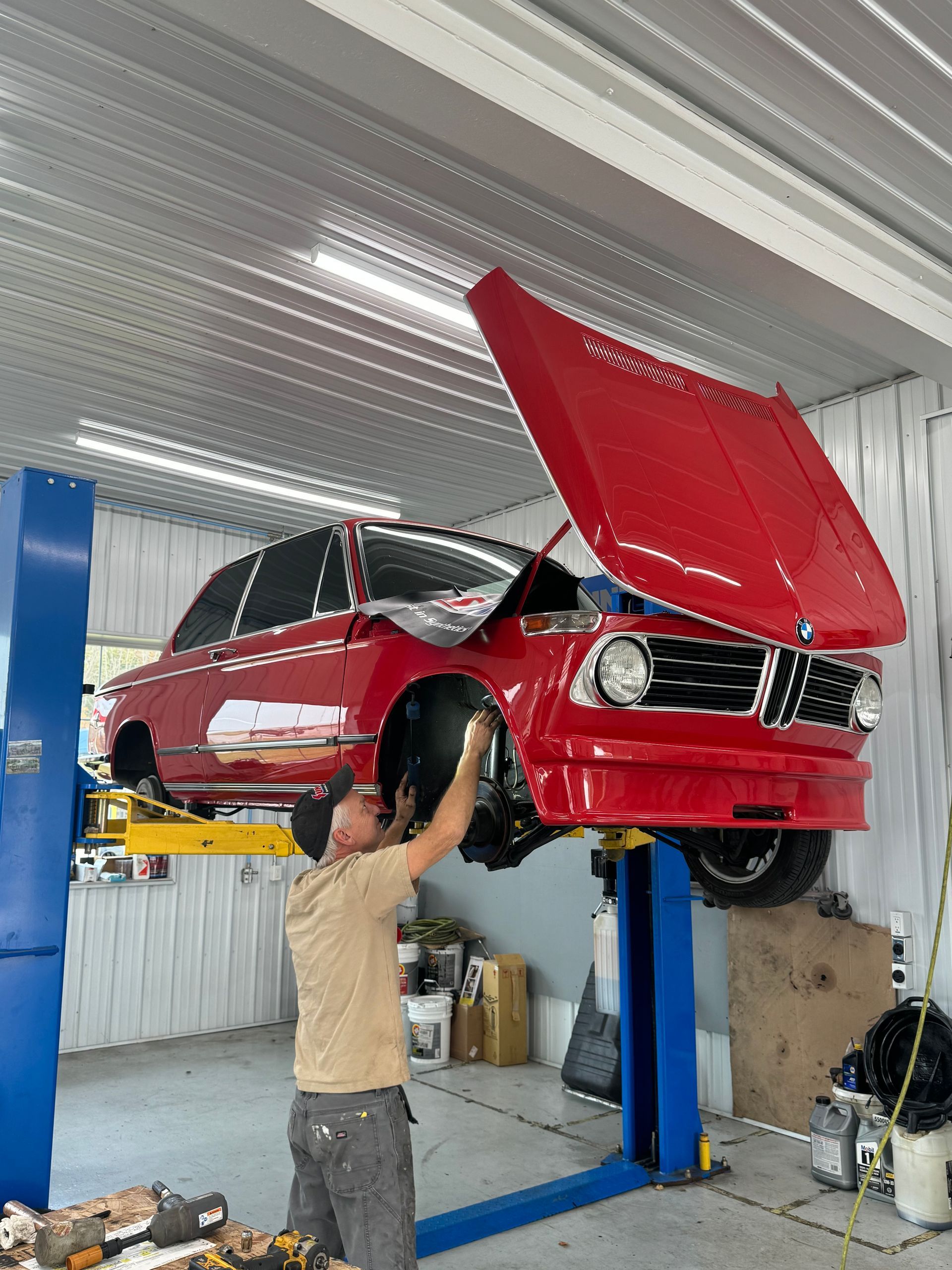 Man working on a red vintage BMW car on a lift in a garage.